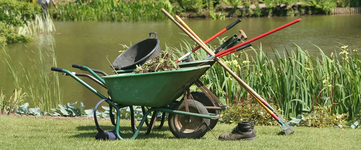 A green wheel barrel with tools for a pond repair in Pensacola
