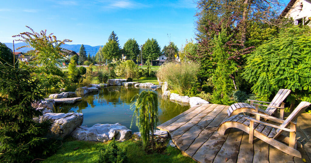 Two Adirondack chairs on a deck overlooking pond