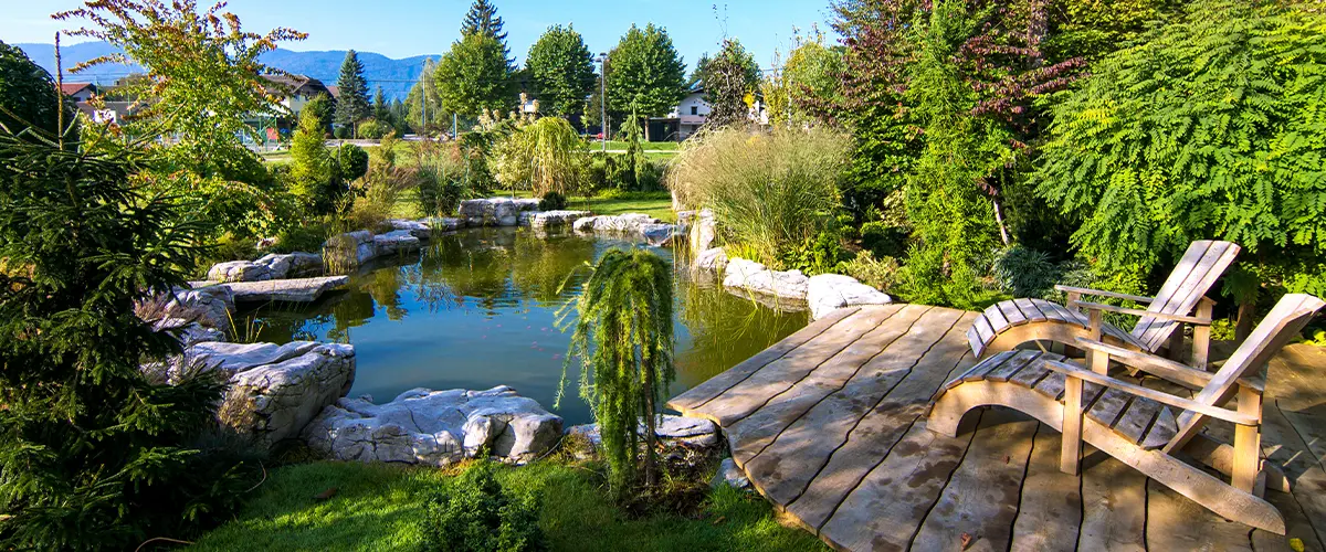 Two Adirondack chairs on a deck overlooking pond